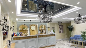 A lobby with a marble floor, a reception desk, chandeliers, and a blue sofa. - Astoria Boutique hotel & SPA (Samarkand)