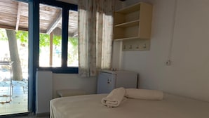A room with a bed, a small table, a cabinet, and a window with curtains. - Kalemi Pansiyon (Marmara)