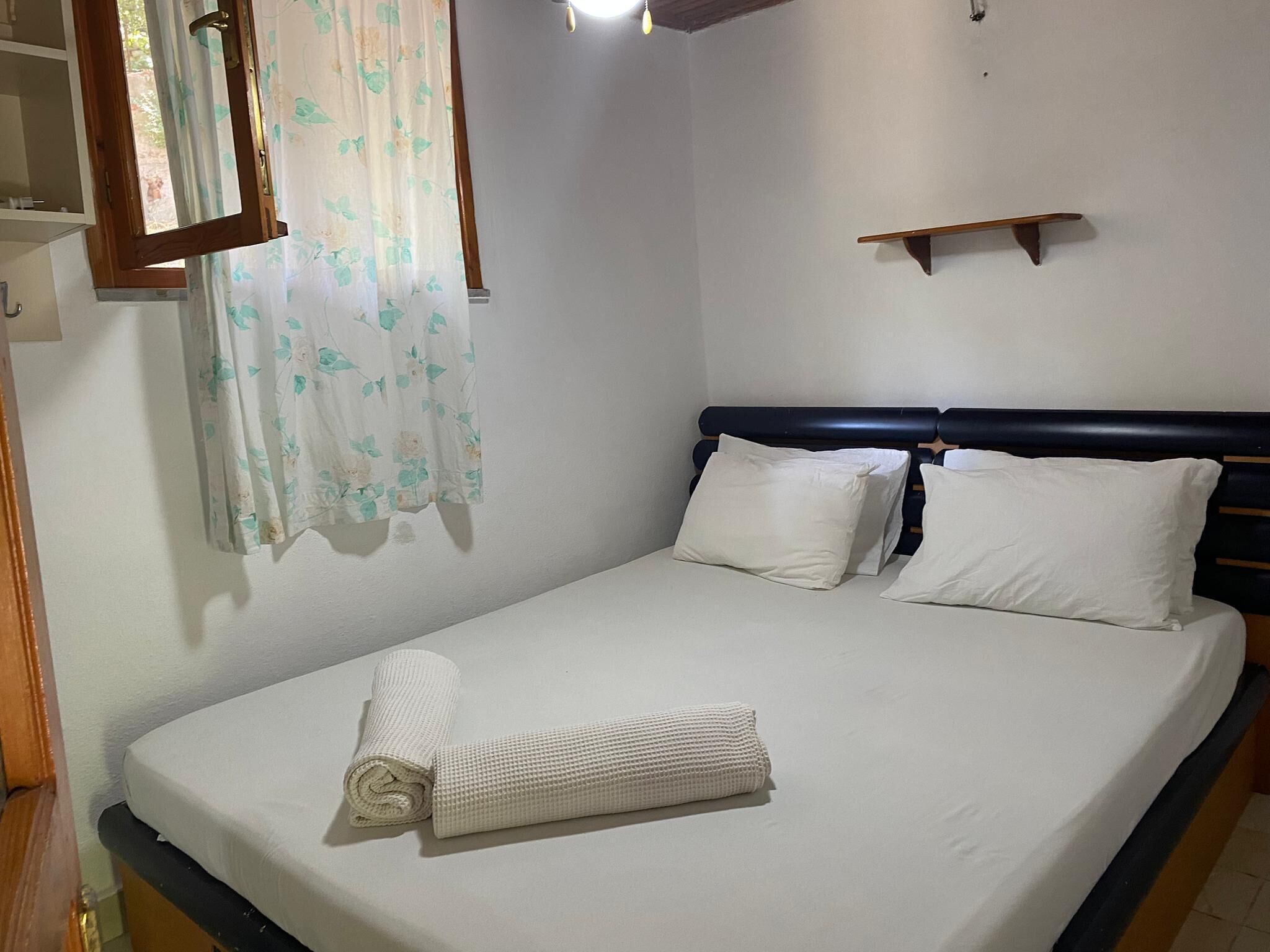 A single bed with white linens, a wooden headboard, and a small wooden shelf above it.