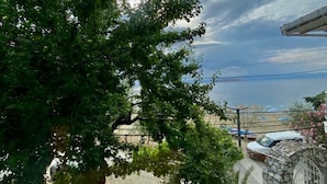 A view of a tree-lined street with a stone building and a parked car. - Kalemi Pansiyon (Marmara)