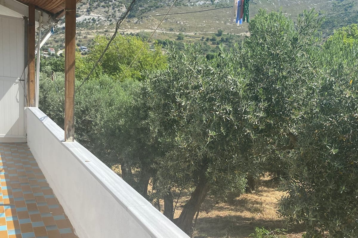 A balcony with a tiled floor, overlooking an olive grove and a hilly landscape.