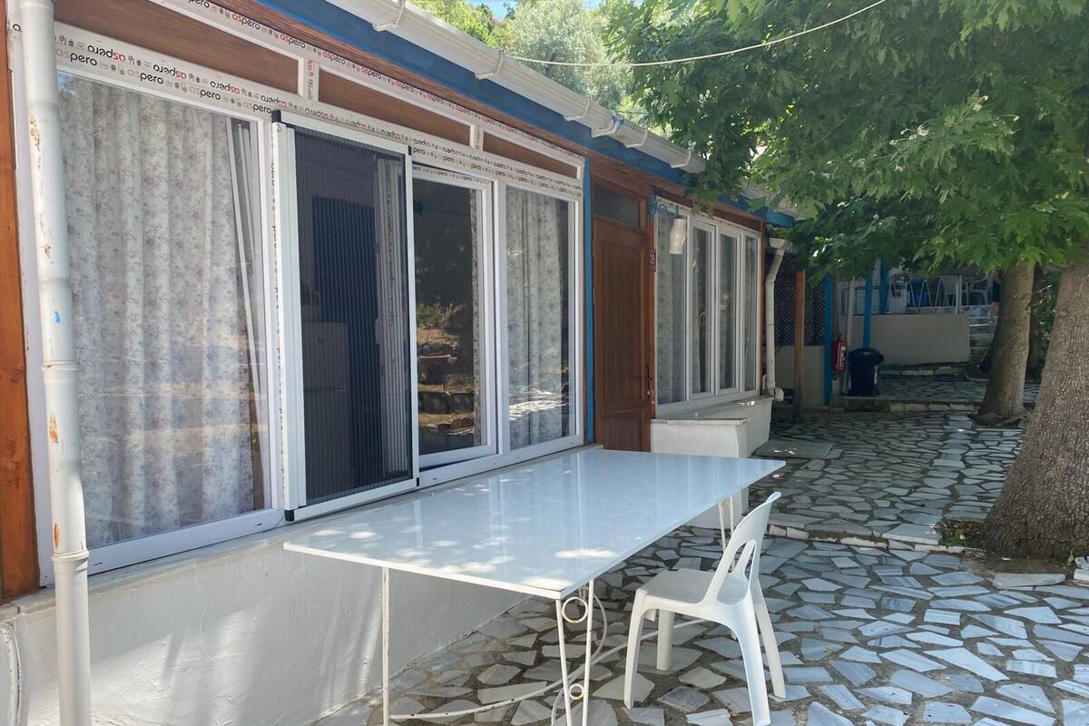 A patio area with a white table and chairs, a tiled floor, and a building with large windows and a wooden door.
