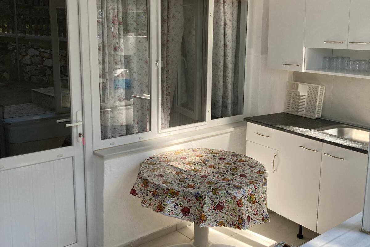 A small kitchen with a round table, white cabinets, a window with curtains, and a number '2' sign.