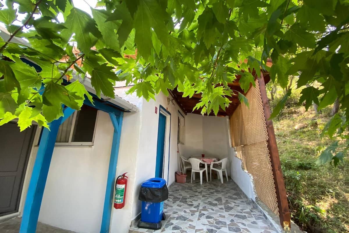 A small patio area with a tiled floor, a table with chairs, a fire extinguisher, and a trash bin.