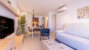 En moderne stue med sofa, fjernsyn, spiseområde og en stor plante.