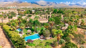 Un complexe hôtelier doté d’une piscine entourée d’une végétation luxuriante et de palmiers, le tout situé au pied de montagnes.