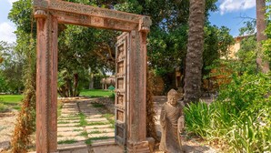 Un arc en bois richement décoré, qui mène à un sentier bordé d’une végétation luxuriante et surmonté d’une statue de Bouddha.