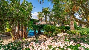 Un jardin luxuriant avec une piscine, des palmiers et des plantes en fleurs.