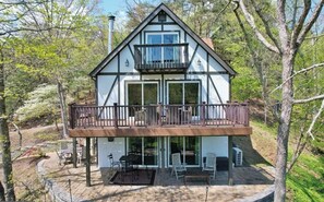 Une maison à deux étages dotée d’un balcon, de grandes fenêtres et d’un patio aménagé avec du mobilier d’extérieur.