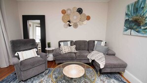 A living room with a grey sofa, a grey armchair, a round coffee table, and a wall art piece above the sofa.