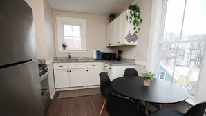 A kitchen with white cabinets, a black refrigerator, a microwave, and a dining table with four chairs.