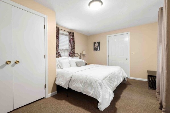 A bedroom with a bed, a wardrobe, a door, and a window with curtains.