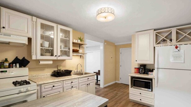 Una cocina con armarios blancos, encimera de granito, estufa, lavabo y refrigerador.