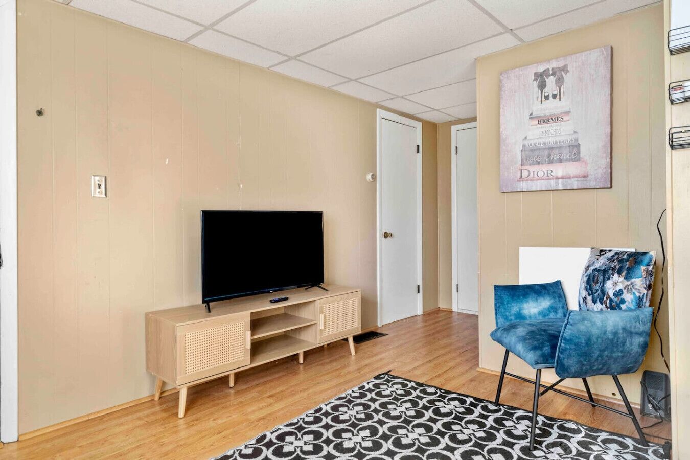 Ein Wohnzimmer mit einem Flachbildfernseher auf einem Holzboden, einem blauen Sessel, einem gemusterten Teppich und einer Wand mit einem gerahmten Bild.