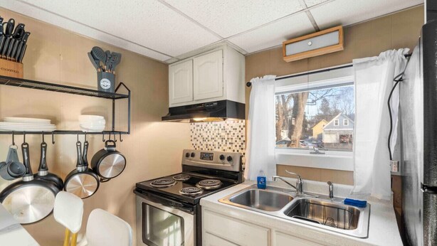 Een kleine keuken met een kookplaat, oven en spoelbak, met een raam en uitzicht op buiten.