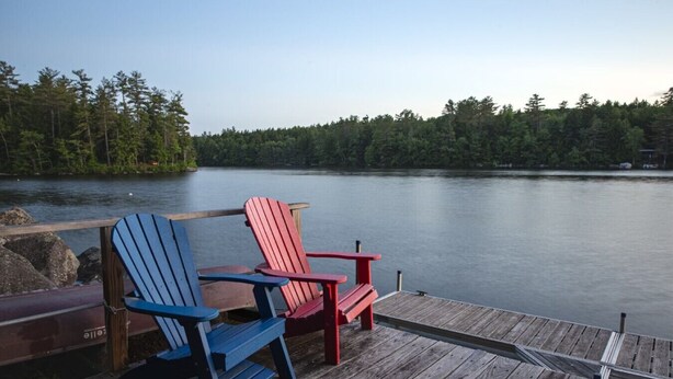A wooden dock with two Adirondack chairs facing a calm lake surrounded by dense forest. - Belgrade Lake house with Dock! (Rome)