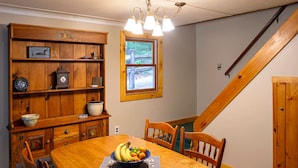 A dining area with a wooden table, chairs, a fruit bowl, a wooden cabinet, and a window with a view. - Belgrade Lake house with Dock! (Rome)