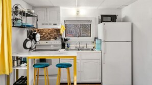 A compact kitchen with white cabinets, a stove, a sink, and a refrigerator. There are two stools and a window with a view of the outside. - Nothing Fancy Older Apt~Walk to Downtown~ King Bed (Dover)