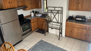 A compact kitchen with wooden cabinets, stainless steel appliances, and a small dining area. - Swampscott! Walk Dtwn and beach (Swampscott)