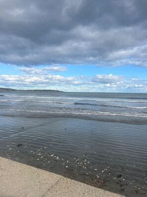 Una playa con olas, cielo nublado y una costa distante.