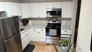 A modern kitchen with white cabinets, stainless steel appliances, and a glass table with a plant. - Dwtn Apt~King Beds~Mins to Salem (Beverly)