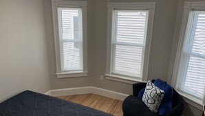 A room with a bed, a chair, and three windows with blinds. - Dwtn Apt~King Beds~Mins to Salem (Beverly)