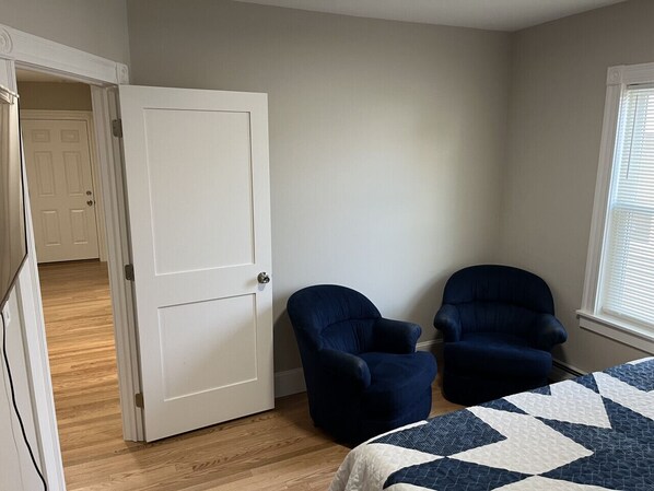 A bedroom with a bed, two armchairs, a door, and a window.