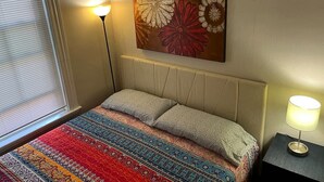 Een slaapkamer met een bed, twee bedlampen, een raam met zonwering en een bloemistisch kunstwerk aan de muur.