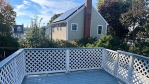 A wooden deck with white lattice railings, surrounded by greenery and a house in the background. - Beverly/Salem! Dwtn/Water/Train (Beverly)