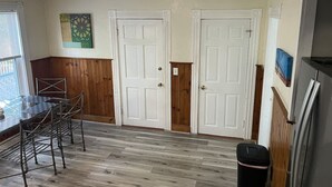 A room with wooden flooring, white doors, a metal rack, a trash bin, and a refrigerator. - Beverly/Salem! Dwtn/Water/Train (Beverly)