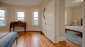 A bedroom with hardwood flooring, a bed with a blue patterned bedspread, a wooden desk, and a white door. - Central Beverly! 5 min to Salem! (Beverly)