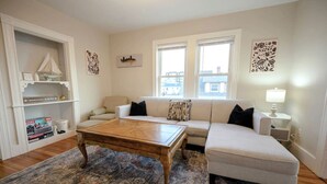 A living room with a sofa, ottoman, coffee table, and a patterned rug. - Central Beverly! 5 min to Salem! (Beverly)