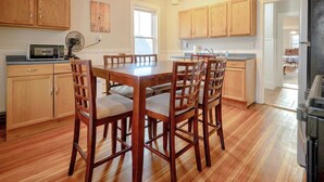 A kitchen with wooden cabinets, a dining table with chairs, a microwave, and a refrigerator. - Central Beverly! 5 min to Salem! (Beverly)