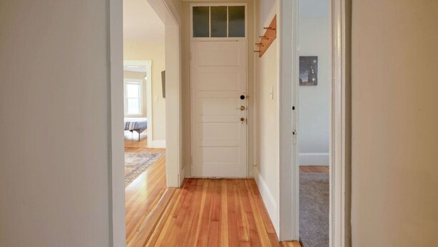 A hallway with wooden flooring leading to a white door with a small window above it. - Central Beverly! 5 min to Salem! (Beverly)