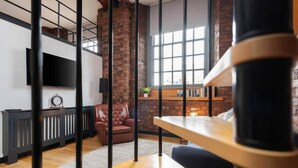 A modern living room with a brick wall, a leather sofa, a wooden table, and a bookshelf. - Liverpool Warehouse Flat | Great Location | Sleeps 5 | WiFi & Free Parking (Liverpool)