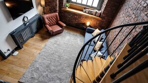 A modern living room with a fireplace, a comfortable sofa, a leather armchair, and a TV mounted on the wall. - Liverpool Warehouse Flat | Great Location | Sleeps 5 | WiFi & Free Parking (Liverpool)