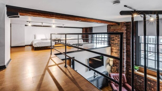 A modern loft-style bedroom with a mezzanine, large windows, and exposed brick walls. - Liverpool Warehouse Flat | Great Location | Sleeps 5 | WiFi & Free Parking (Liverpool)
