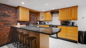 A modern kitchen with wooden cabinets, a granite countertop, and a brick accent wall. - Liverpool Warehouse Flat | Great Location | Sleeps 5 | WiFi & Free Parking (Liverpool)