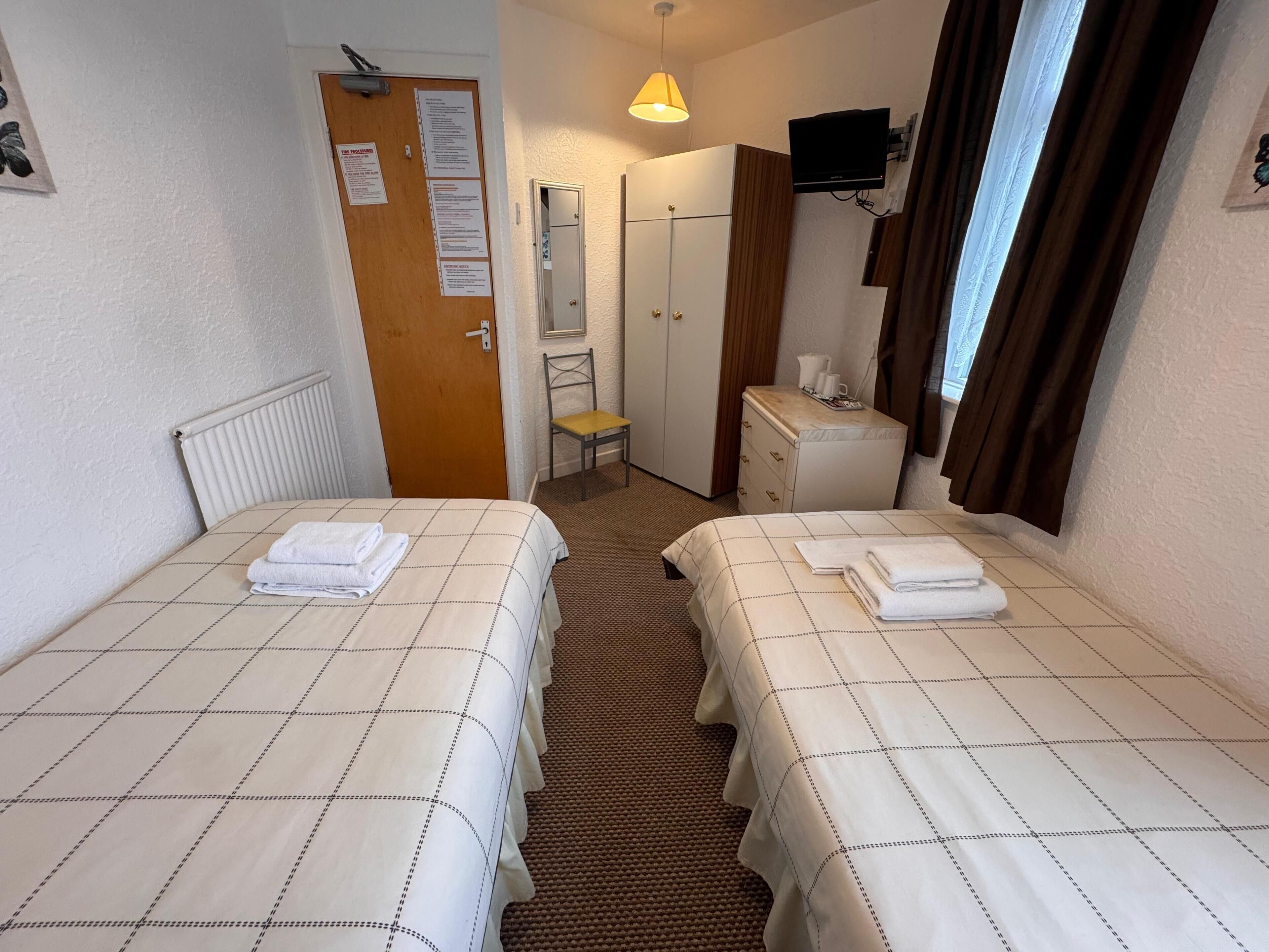 A hotel room with two beds, a dresser, a mirror, a television, and a window with curtains.