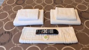 Un lit bien fait, avec une couvre-lit à motifs, deux serviettes pliées et une télécommande.