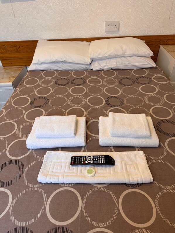 A neatly made bed with a patterned bedspread, two folded towels, and a remote control.