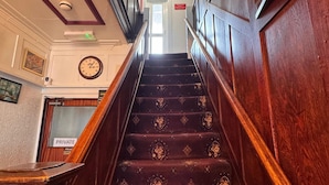 Un escalier en bois recouvert d’une moquette à motifs, menant à une porte portant l’inscription « PERSONNEL ».