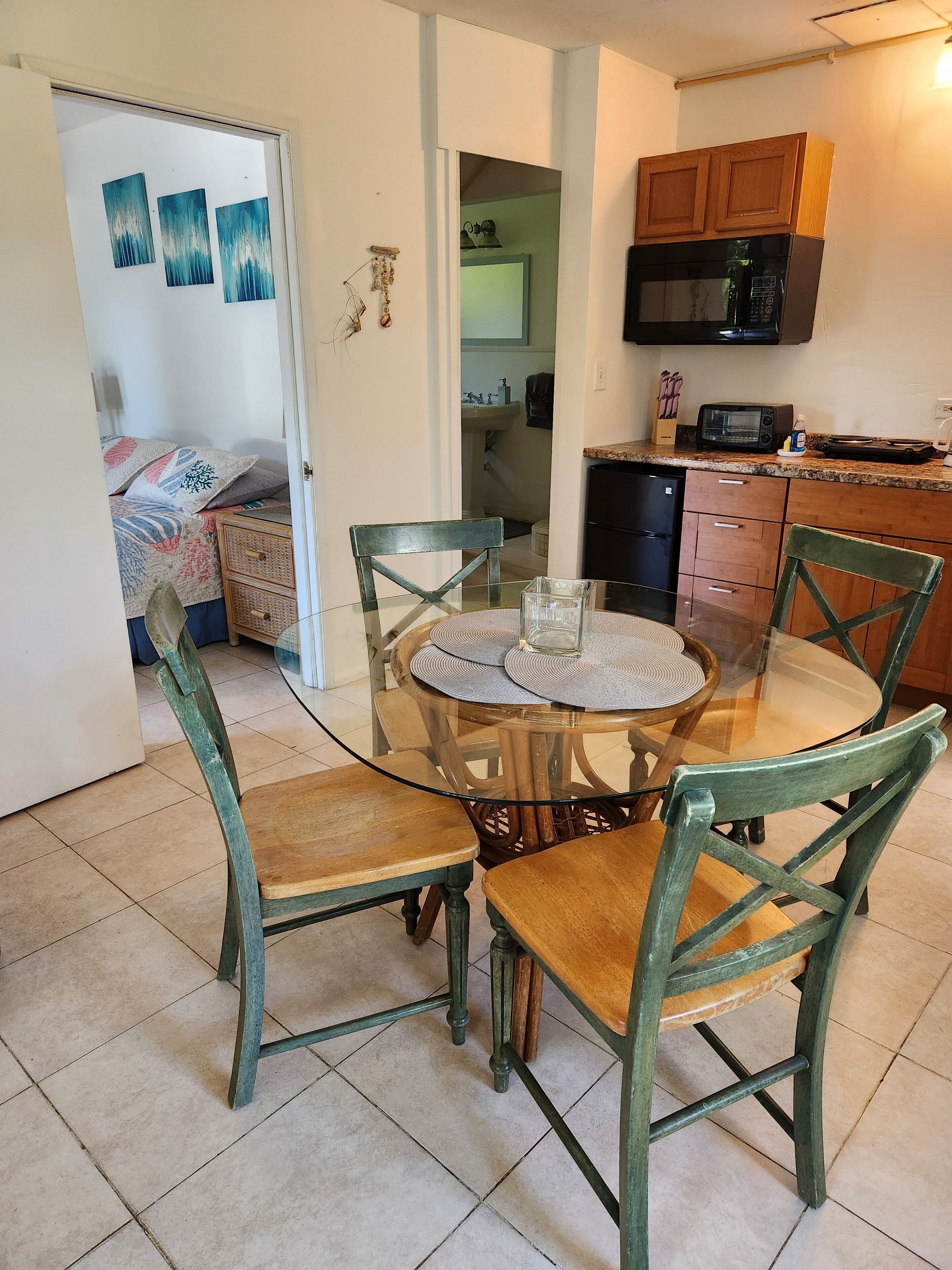 Un comedor con una mesa redonda de vidrio, sillas verdes y una cocina al fondo.