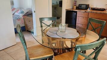 Un comedor con una mesa redonda de vidrio, sillas verdes y una cocina al fondo.
