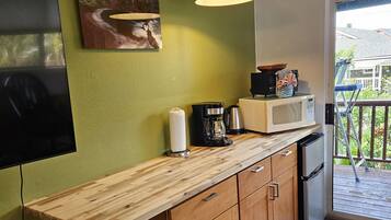 A compact kitchen with a wooden countertop, a microwave, a coffee maker, and a hanging light fixture.
