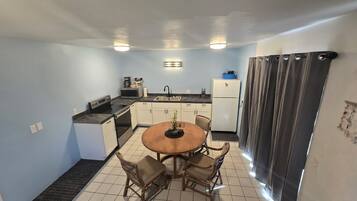 A compact kitchen with a dining table, chairs, a refrigerator, and a microwave.