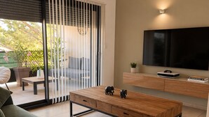 Una sala de estar moderna con sofá, mesa de centro, televisor y puertas corredizas de vidrio que dan a un área exterior.
