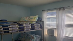 Een slaapkamer met een stapelbed, een plafondventilator, een tafeltje en een raam met zonwering.