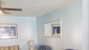 Een woonkamer met een bank, twee fauteuils, een bijzettafeltje, een lamp en ingelijste foto’s aan de muur.