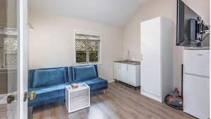 A compact kitchen with a blue sofa, white cabinets, a refrigerator, and a window with a view of greenery. - Serene 2BR Home w Grill & Yard by Zodiak Stays (Auckland)